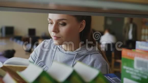 年轻的白种人美丽的女学生正站在书架附近书在宽敞的图书馆里拿着一本转过身来视频的预览图