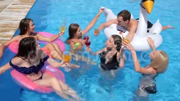 泳池派对公司的年轻人戴着带酒精饮料的充气戒指在泳池边度暑假视频的预览图