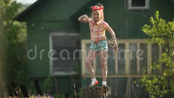 一个可爱的小女孩在乡间房子的院子里的树桩上跳舞很开心视频的预览图