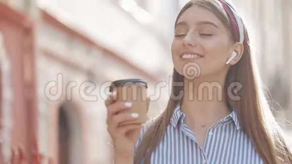漂亮的年轻白种人女孩棕色头发头戴条纹衬衫戴着耳机微笑着喝酒视频的预览图