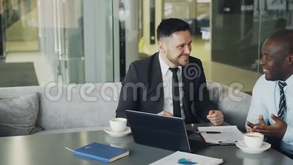 两个商人在现代咖啡馆里谈笑风生商务同事在看手提电脑时玩得很开心视频的预览图