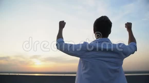 在日落背景下高加索人举起双手朝天空的后景动机视频的预览图