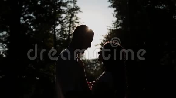 一对相爱的夫妇在日落的背景下拥抱和亲吻阳光穿过他们的脸视频的预览图