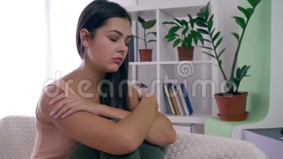 忧郁的女人沮丧的女人坐在家里明亮的房间里的沙发上视频的预览图