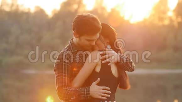 家庭和关系的概念年轻的情侣在夕阳下拥抱视频的预览图