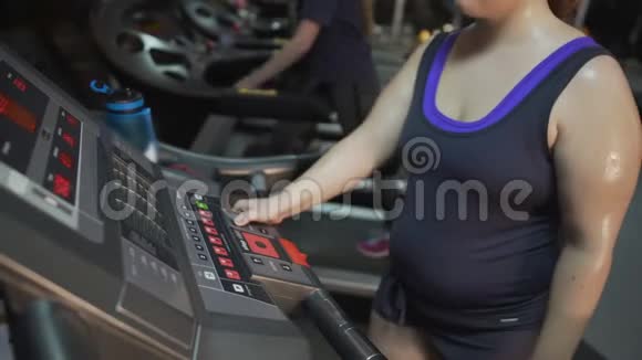 超重女士在跑步机面板上按按钮开始健身视频的预览图