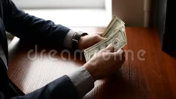 一个商人一张桌子上数着一百美元的钞票手里拿着手表和木头桌子上的美元金融概念视频的预览图