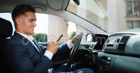 年轻英俊的商人在车里用手机快乐的年轻人成功并写了一条信息的概念视频的预览图