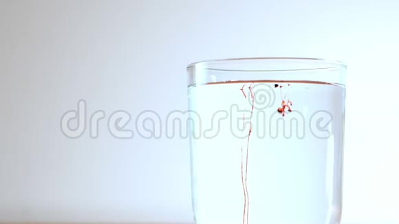 红色物质的小颗粒落入透明的水玻璃中溶解并留下长长的痕迹视频的预览图