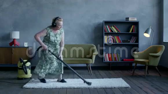 快乐的老年妇女听耳机音乐用吸尘器跳舞家庭乐趣视频的预览图