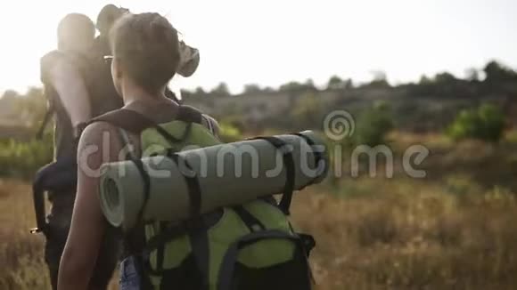 两个旅行者男人和女人带着巨大的背包正在徒步旅行在草山边散步太阳照耀着背景视频的预览图