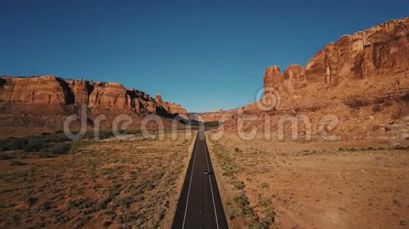 汽车沿美国沙漠公路直线行驶在大气岩石山峡谷山脊之间的空中镜头视频的预览图