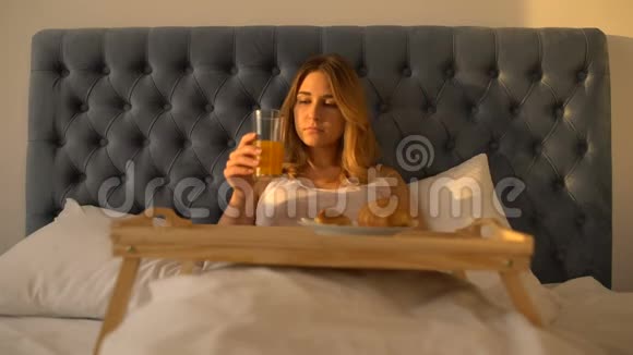 女人吃新鲜的面包在床上喝橙汁健康的早晨食品视频的预览图