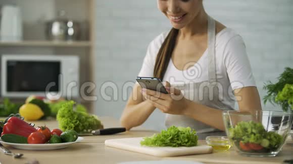 微笑的亚洲女孩在做饭前看智能手机的视频食谱视频的预览图