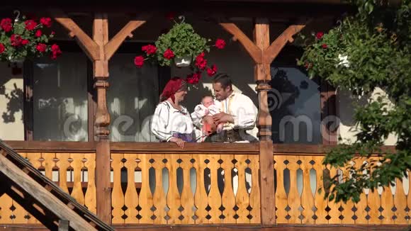 在木屋阳台上穿传统衣服的男人女人和婴儿父母亲吻孩子家庭肖像视频的预览图