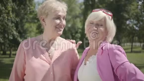 两个积极的老女人看着相机微笑站在夏季公园的肖像户外休闲女朋友视频的预览图