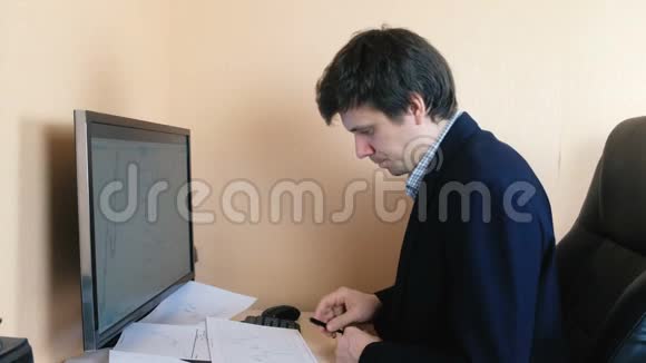 沮丧的男人在电脑前工作打电话给手机在屏幕上和纸上比较图形视频的预览图