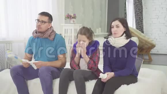 一家人感冒了爸爸妈妈和女儿坐在家里的床上打喷嚏视频的预览图