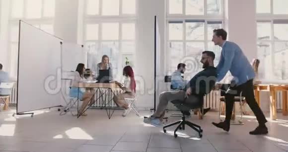 侧景拍摄两个疯狂有趣的男性商人骑着办公椅沿着大空地大厅庆祝胜利视频的预览图