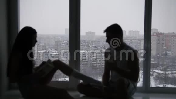 白雪皑皑的冬日一对幸福的年轻夫妇坐在窗前的剪影视频的预览图