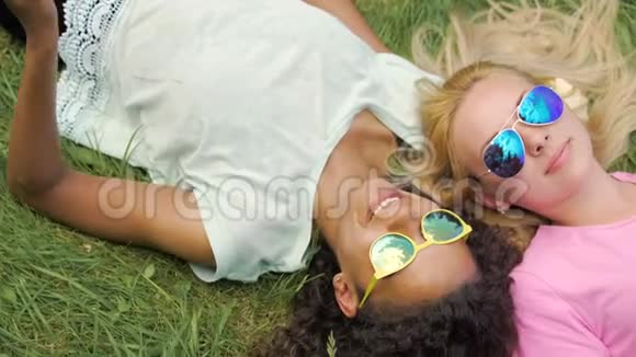 两个女孩最好的朋友躺在草坪上用手机拍照在公园里玩得很开心视频的预览图