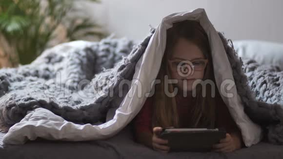 可爱的女孩躺在毯子和触摸垫下面视频的预览图