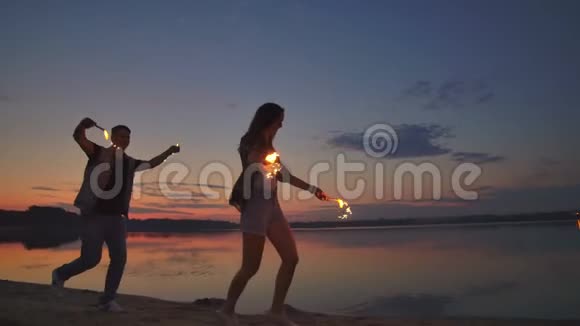 年轻的恋人们男人和女人欢快地沿着海滩奔跑手里拿着热闪闪发光的腐烂物动作缓慢浪漫浪漫视频的预览图