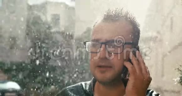 愤怒的戴着眼镜的人在雨中用手机说话时对某人大喊大叫的肖像4K录像视频的预览图