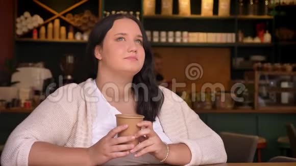 一个爱做梦的白种人女人在咖啡馆里思考和拿着她的饮料视频的预览图