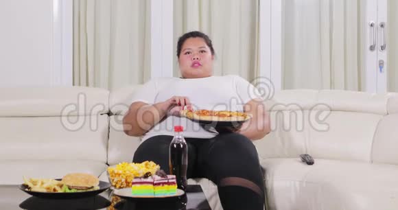 超重的女人在沙发上吃披萨视频的预览图