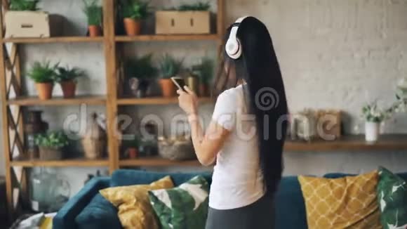 慢动作快乐的亚洲女孩学生戴着耳机拿着智能手机听音乐跳舞和视频的预览图