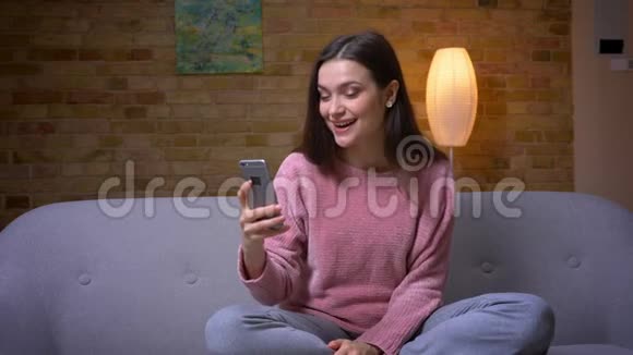 一位年轻漂亮的黑发白种人女性的特写镜头她在电话上打了一个视频电话坐在那里微笑着视频的预览图