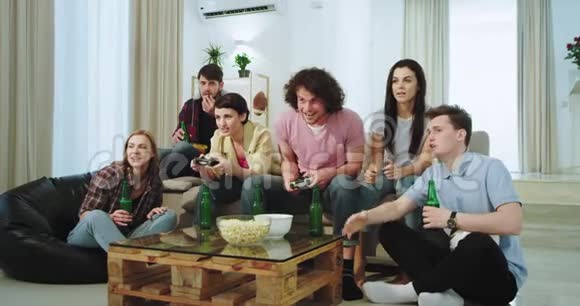 非常兴奋的多民族朋友在客厅里看他们的两个朋友是如何在一个电子游戏中其中一些人视频的预览图