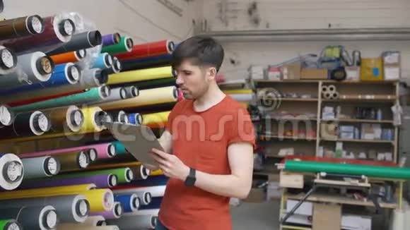 年轻工人在仓库的多利镜头与剪贴板检查库存男子在广告销售部工作视频的预览图