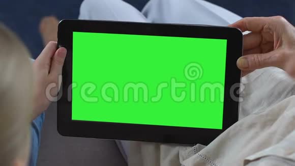 孙女在绿色屏幕平板电脑上展示奶奶的移动应用程序信使视频的预览图