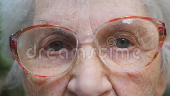 戴眼镜的老妇人看着摄像机一位有皱纹的老太太的眼睛特写肖像画视频的预览图