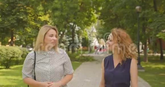 两位女性朋友在公园里散步开心地微笑着交谈视频的预览图