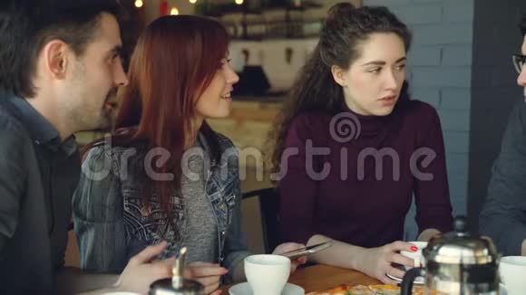 开朗的年轻人和女性亲密的朋友正在使用智能手机和交谈同时在漂亮的咖啡馆吃午饭用餐视频的预览图