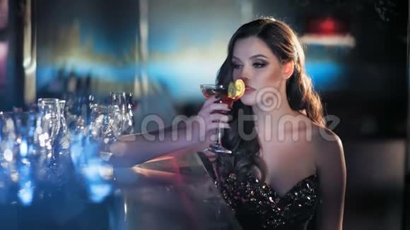 美丽的年轻黑发女人坐在酒吧里在豪华的内部喝着一杯酒视频的预览图