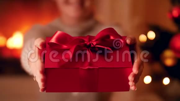 特写4k视频年轻女子手持漂亮的红色礼盒大丝带并在圣诞树旁边鞠躬视频的预览图