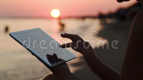 日落时分在海滩上玩平板电脑的女孩视频的预览图