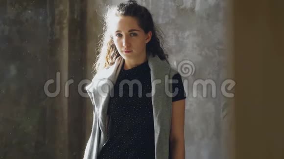 一幅迷人的年轻女孩静静地站在里面看着相机的肖像在阳光明媚的房间里视频的预览图