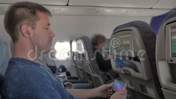 一个男人戴着耳机看视频在手机上听音乐坐在飞机上视频的预览图