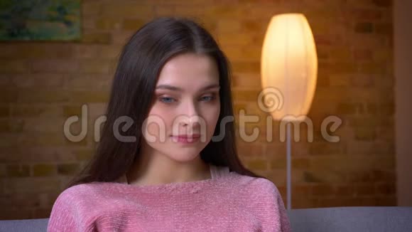 一个年轻可爱的黑发白种人女孩在一个舒适的沙发上坐着看着摄像机开心地笑着特写镜头视频的预览图