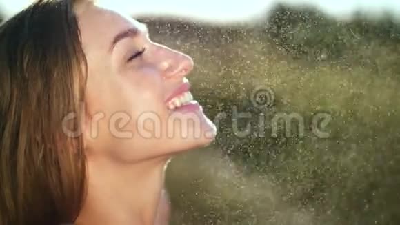 一个性感美丽的金发女孩的肖像在一场小雨下在阳光下在一片绿色的草地上女孩视频的预览图