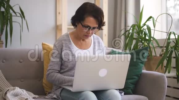 戴眼镜和灰色开襟羊毛衫写短信的老妇人视频的预览图