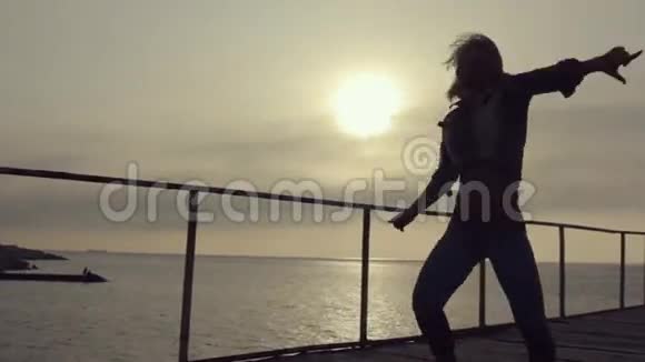 夕阳西下一个身材矮小的女孩在海边的码头上翩翩起舞视频的预览图