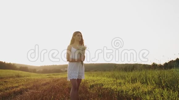 穿着白色连衣裙的漂亮女孩站在田野里手捧鲜花望着晴朗的夜空视频的预览图