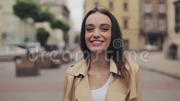 穿着壕沟的迷人少女站在城市背景的近旁看着幸福的微笑和欢笑视频的预览图