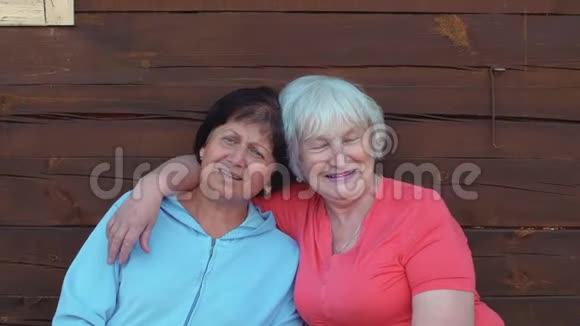 两个快乐的高级妇女在木墙旁拥抱和唱歌视频的预览图